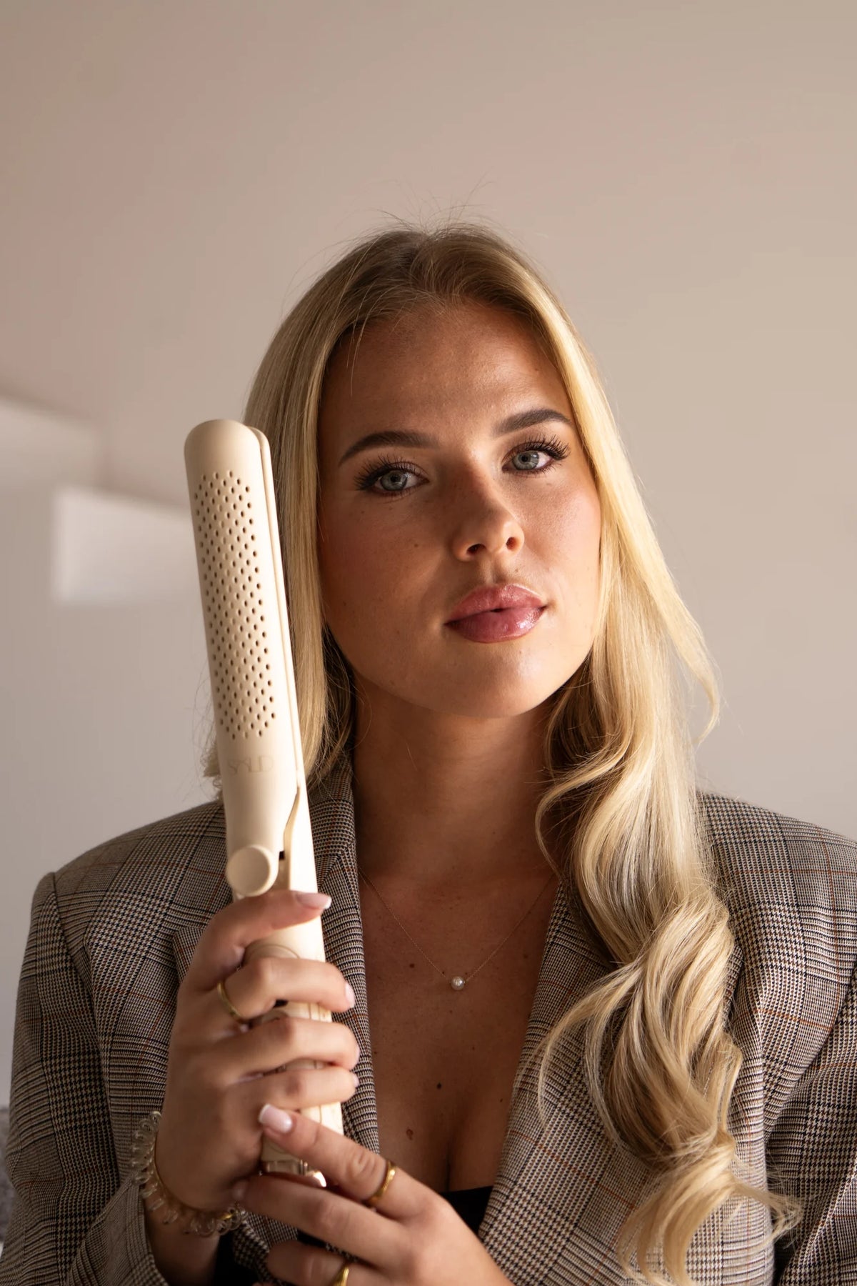 Model met lange blonde krullen houdt de beige SOLID haarstyler vast.